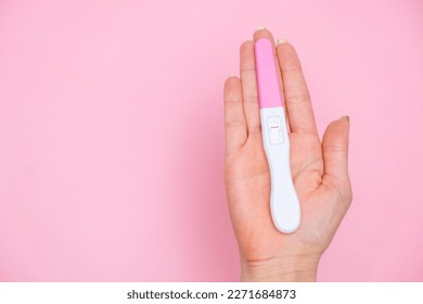 Female hand holding a negative pregnancy test on the pink background with copy space. 