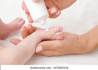  Female hand holding newborn leg on white towel. Mother applying medical ointment on dry skin. First days after birth. Care about baby clean and soft body skin. Close up.
