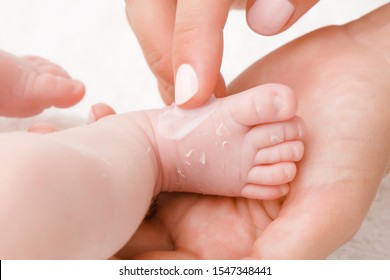 Female Hand Holding Newborn Leg. Mother Carefully Applying Medical Ointment On Dry Skin. First Days After Birth. Care About Baby Clean And Soft Body Skin. Close Up.