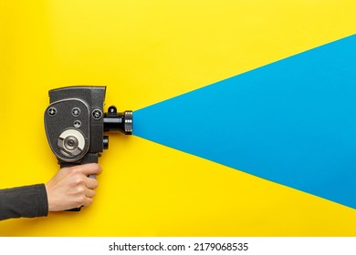 Female hand holding old style film movie camera on a yellow background with blue ray coming out of the camera,  imitating shooting process. Ukrainian flag colors. Film making industry concept - Shutterstock ID 2179068535