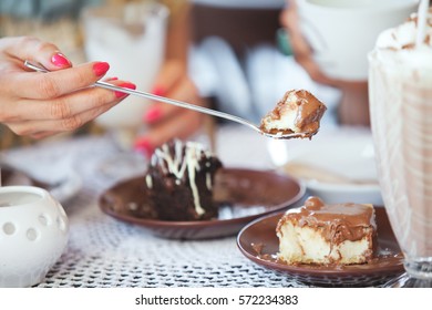 Female Hand Holding On Long Spoon A Piece Of Cake At Table In Cafe