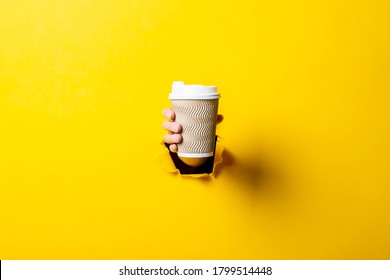 Female Hand Holding A Paper Cup Of Coffee On A Bright Yellow Background.