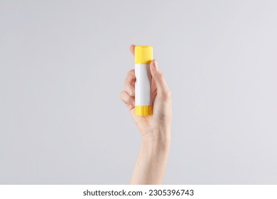 Female hand holding paper glue stick on gray background - Shutterstock ID 2305396743