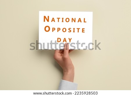 Female hand holding paper sheet with text NATIONAL OPPOSITE DAY on light background