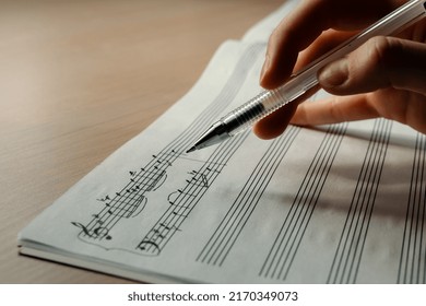 Female Hand Holding A Pen On The Background Of Music, Writing Music, Hand Writing Notes, Selective Focus