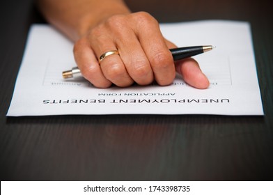 A Female Hand Holding A Pen Over The Unemployment Benefits Form To Fill. Crisis, Stress, Jobless Abstract.