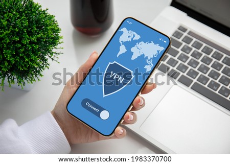 female hand holding phone with app vpn on screen over table with laptop in office