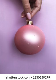 Female hand holding a pink christmas sphere on lilac background