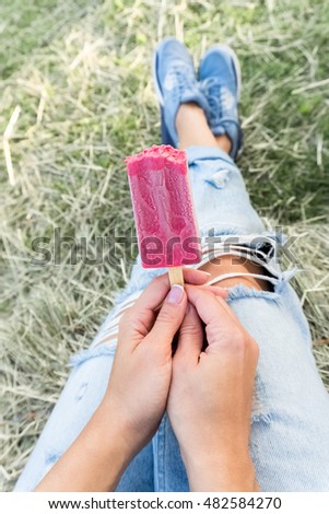female hand holding pink ice cream fruit on a grass background. the view from the top
