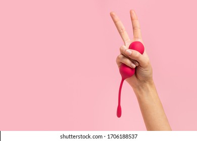 Female hand is holding pink Kegel balls and showing victory sign on a pink background. Vaginal balls in the hand of a woman. Sex toys Geisha balls. Place for text. Sex shop concept. Copy space