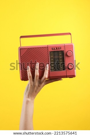 Female hand holding a pink retro radio receiver on a yellow background