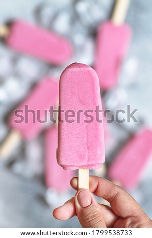 Female hand holding pink strawberry popsicle ice cream. Pastel colors. Top view