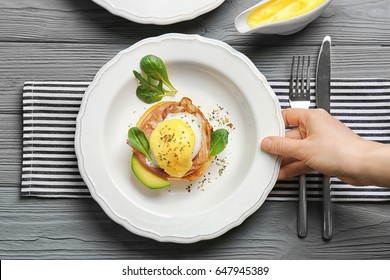 Female Hand Holding Plate With Egg Benedict, Top View