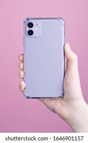 Female Hand Holding Purple IPhone 11 In Clear Silicone Case Isolated On A Pink Background. Clear Phone Case Mock Up Back View