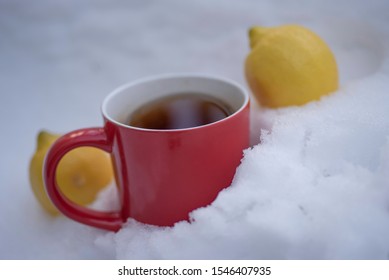 Female Hand Holding Red Cup Of Tea Buried In Snow Next To Two Lemons.  Vitamin C And Tea Antioxidants As Prevention Of Flu Season Concept. 