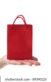 Female Hand Holding Red Gift Bag With Present With Her Fingers - Shopping And Holiday Concept