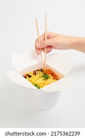 Female Hand Holding Rice Wok With Wooden Chopsticks, Asian Chinese Wok Isolated On White Background. One Open Takeout Box With Wok, Seafood Cocktail And Vegetables. Fast Food Delivery Concept
