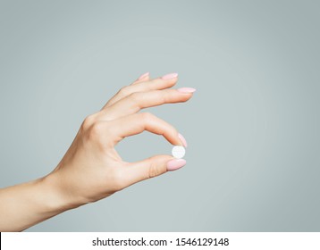 Female hand holding a round white medical pill or vitamin.