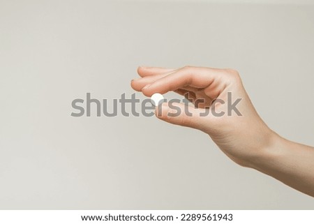 female hand holding a round white pill on a gray background