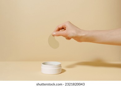 Female hand holding sample of green algae extract eye patch over white jar of product on beige isolated background. The concept of natural product for moisturizing, from dark circles and wrinkles - Powered by Shutterstock