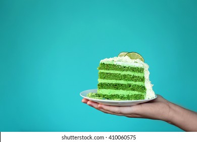 Female Hand Holding Saucer With Piece Of Delicious Creamy Lime Cake On Blue Background