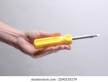 Mano femenina que sostiene el destornillador sobre fondo gris