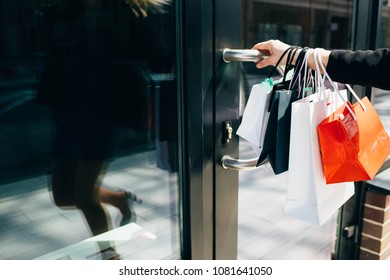 Female Hand Holding Shopping Bags And Open Door Of Shop