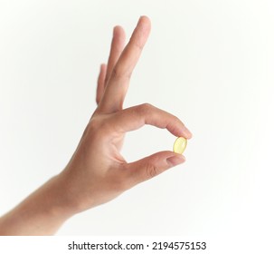 Female Hand Holding A Show Clear Yellow Pill Capsule On A White Background