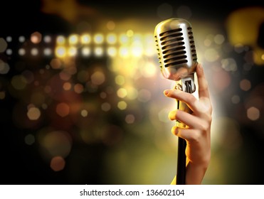 Female hand holding a single retro microphone against colourful background