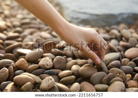 female hand holding small pebble stones picking up pebbles, round shape pebbles, summer vacation souvenir,