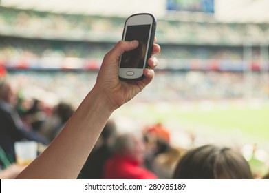 A Female Hand Is Holding A Smart Phone In A Stadium To Take Pictures Of A Sporting Event