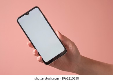 Female Hand Holding Smartphone With Blank Screen Over Pink Background. Phone Mockup.