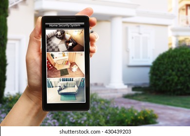 Female hand holding a smartphone on blurred house background. Home security system concept