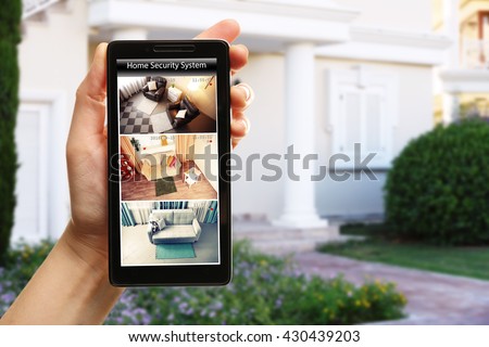 Female hand holding a smartphone on blurred house background. Home security system concept