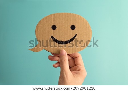 Female hand holding a smiley face speech bubble paper cute against green background.
