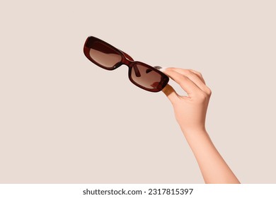 Female hand holding stylish sunglasses on white background