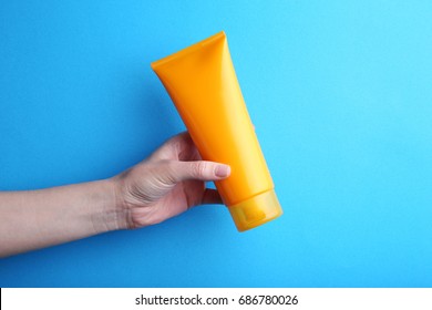 Female Hand Holding Sunscreen Cream On Blue Background