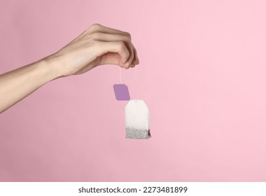 Female hand holding tea bag with label on pink background