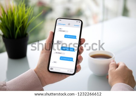 female hand holding touch phone with app messenger on the screen above the table in cafe
