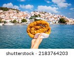 A female hand is holding a traditional, local cheese pie so called Tyropitta in front of the city of Skopelos island, Sporades, Greece
