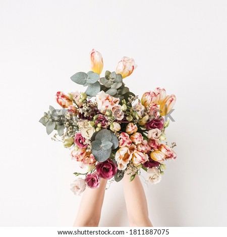 Female hand holding tulip, eucalyptus flowers bouquet against white wall. Holiday celebration festive floral concept