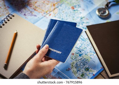 Female Hand Holding Two Passports On A Background Map. Compass, Notepad, Pencil And Book.