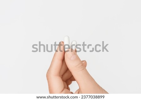 female hand holding two white capsules on a white background. taking medication, health care concept