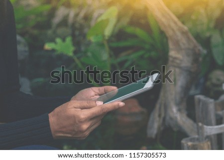 Female hand holding and using digital tablet  while sitting in the garden. Internet technology concept .