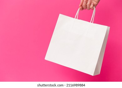 Female Hand Holding White Blank Shopping Bag Isolated On Pink Background. Black Friday Sale, Discount, Recycling, Shopping And Ecology Concept