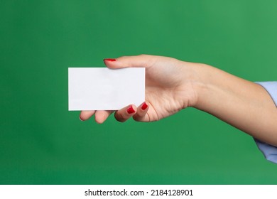 Female hand holding white card on a green background, wearing red nail polish.