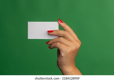 Female hand holding white card on a green background, wearing red nail polish. 