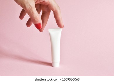 Female Hand Holding White Cosmetic Product Tube. Blank Plastic Container For Cream, Lotion, Toothpaste, Nourishing Or Moisturizing Mask On A Pink Background. Eco-friendly, Organic Cosmetology Concept.