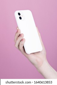 Female Hand Holding White IPhone 11 Back Side View. White Phone Case Mock Up In Female Hand Isolated On Pink Background