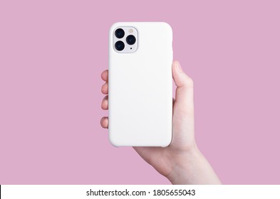 Female hand holding white iPhone 11 Pro in soft silicone white cover back view . Phone case mock up isolated on pink background